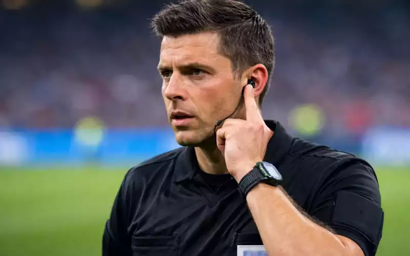 Fodbolddommer med finger på ørestykke kommunikerer med VAR-rummet